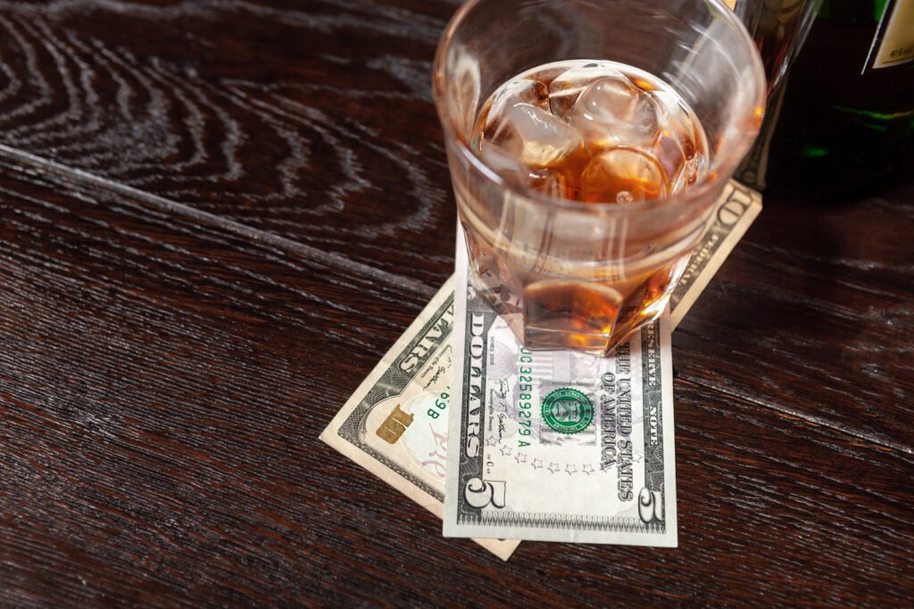 Glass of whiskey and money on the bar counter.